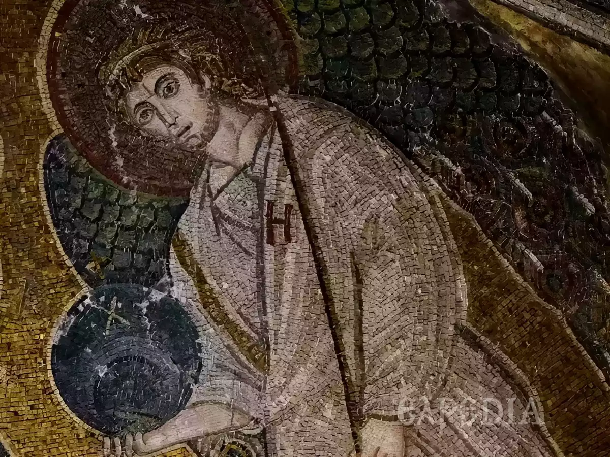 Detail of an archangel from the Panagia Angeloktisti apse mosaic, showing the figure's face and upper body in a light-colored robe, holding a dark sphere against a gold background.