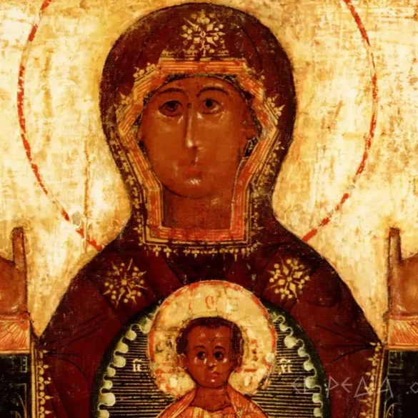 detail of a russian icon depicting the face of the virgin mary with a crown and the infant christ within a medallion on her chest, on a gold background with brown tones.